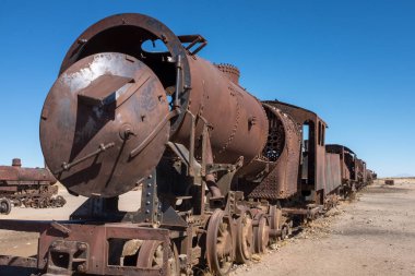 Paslanmış bir buhar treninin ve vagonların manzarası Bolivya 'nın Uyuni kentinin hemen dışındaki tren mezarlığında yavaşça çürüyor.