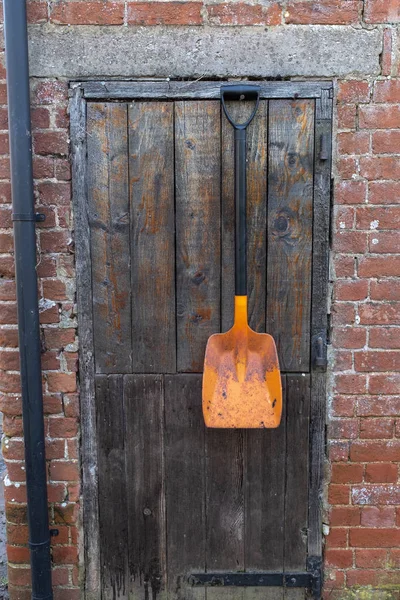 Een schop met een feloranje hoofd die buiten een schuur deur hangt — Stockfoto