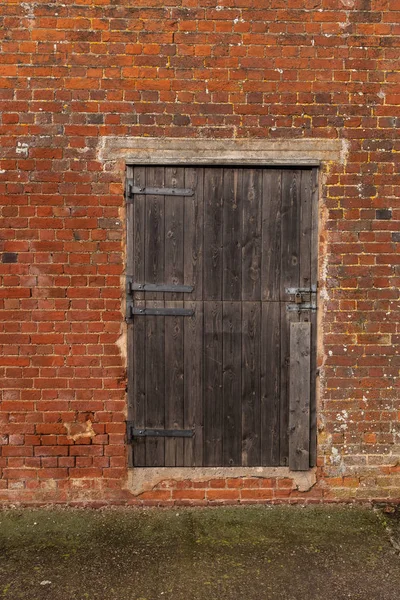 Una puerta de granero de madera sazonada en una pared de ladrillo de un edificio en una granja Fotos de stock
