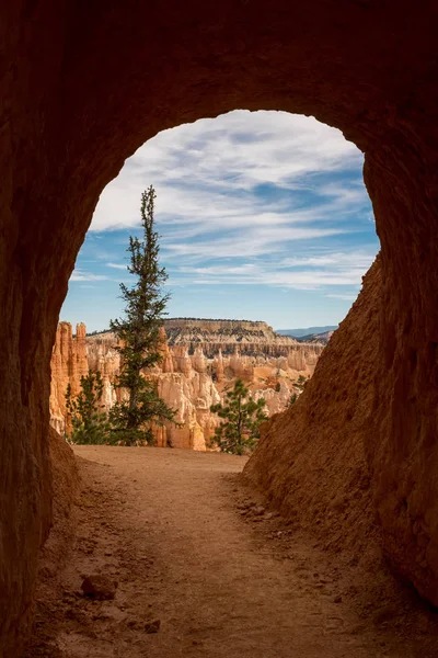 En liten tunnel som skär genom sandsten a den fantastiska Bryce Canyon i slutet av tunneln är en utsikt över kanjonen och de många sandsten hoodoos med olika nyanser av apelsiner och röda — Stockfoto