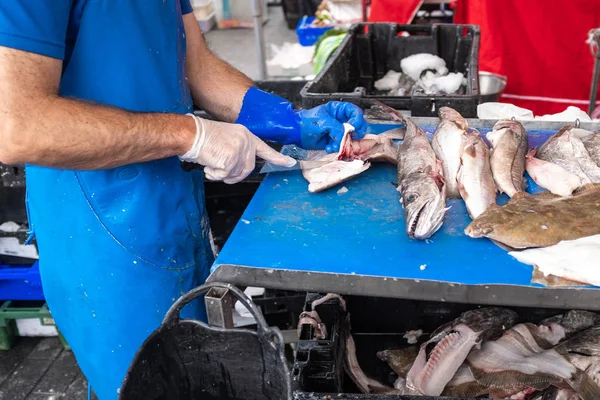 Fish monger filleting a number of fresh fish on market stall. — Stock Photo, Image