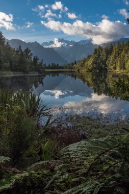 İnanılmaz güzel Matheson Gölü yaprakları ile çerçeveli bir portre görünümü, Çarpıcı Güney Alpleri ve durgun sularda görkemli Mt Cook yansıması ile Yeni Zelanda.