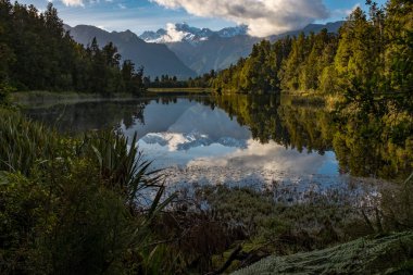 İnanılmaz güzel Matheson Gölü yaprakları ile çerçeveli bir portre görünümü, Çarpıcı Güney Alpleri ve durgun sularda görkemli Mt Cook yansıması ile Yeni Zelanda.