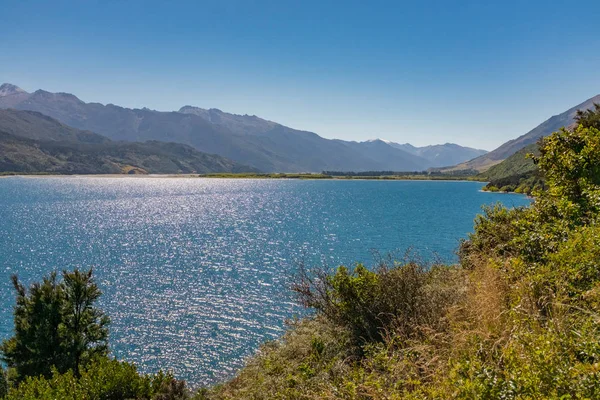 ニュージーランドのオタゴにある自然のままの湖のきらめく海は 澄んだ青空と遠いブッシュランドに対してギザギザの山頂に囲まれています — ストック写真