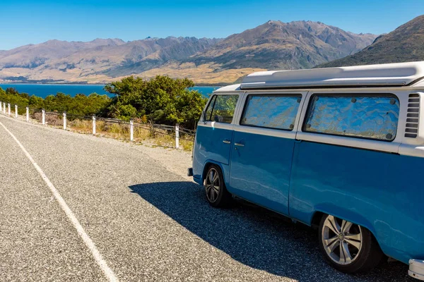 Bir vintage mavi ve beyaz campervan güzel bir göl yakınında park, açık mavi gökyüzüne karşı mesafe dağlar ile
