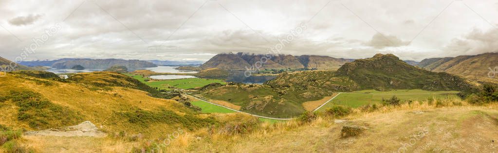 A wide panorama of Wanaka and the surronding hills and lakes taken from the top of the Diamond Lake trail, low clouds hug the hills in the distance