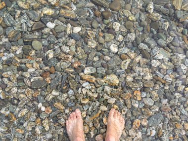 kristal berraklığında göl suyunda renkli çakıl taşları üzerinde duran ayak çifti 