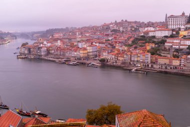 Sabahın erken saatlerinde Porto şehrinden sızan Douro Nehri manzarası. Şafak vakti nehre bağlanmış geleneksel tekneler, alçak bulutlar altında yol alıyorlar.