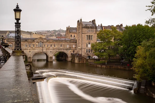 Arka planda tarihi Pulteney Köprüsü olan Bath 'daki Avon Nehri, Weir' ın suyunu yumuşatmak için yavaş panjur hızı.