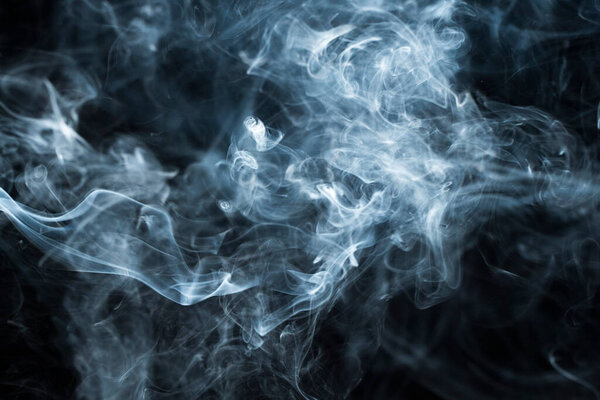 Background image of a wisp of smoke on a dark background. The texture of the flowing smoke. Frozen smoke on a dark background. Graphic resources dark backdrop. Texura of white clouds of fog. Curls of smoke frozen in motion.