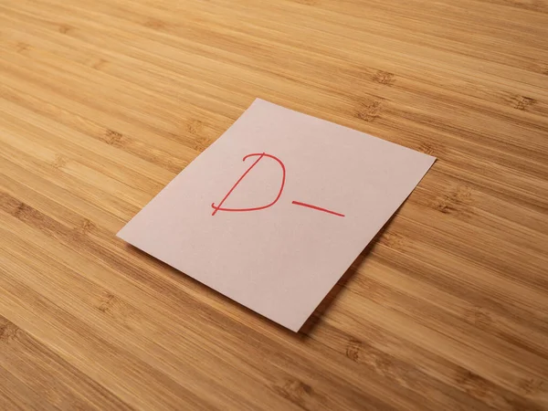 Sticker depicting the letter d. Paper sticker pasted on a wooden surface. Self-adhesive paper sheet. A piece of paper on a wooden board. Reminder for action. Paper sheet for notes.