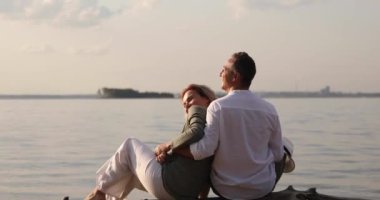 kadın ve erkek batan güneşte deniz tarafından bir kütük üzerinde oturuyor