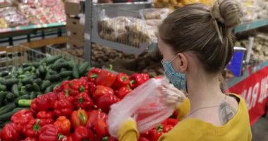 Mağazada maskeli bir kız kırmızı biber seçiyor.