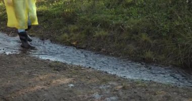 Sarı yağmurluklu ve lastik çizmeli bir kadın su birikintilerinde zıplıyor.