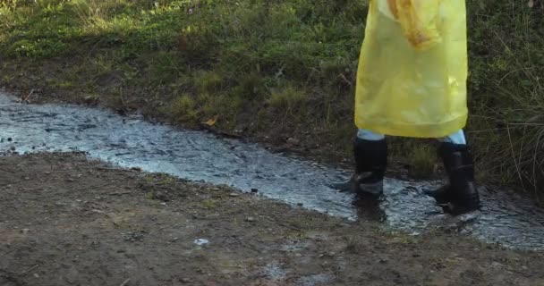 黄色のレインコートとゴム製のブーツを着た女性が水溜りを飛び越えて — ストック動画