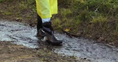 Sarı yağmurluklu ve lastik çizmeli bir kadın su birikintilerinde zıplıyor.