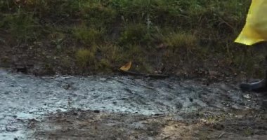 Sarı yağmurluklu ve lastik çizmeli bir kadın su birikintilerinde zıplıyor.