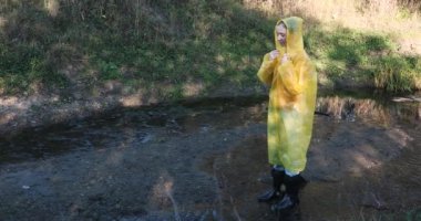 Sarı yağmurluklu ve lastik çizmeli bir kadın su birikintilerinde zıplıyor.