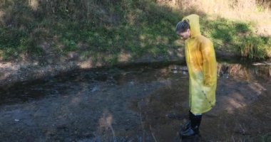 Sarı yağmurluklu ve lastik çizmeli bir kadın su birikintilerinde zıplıyor.