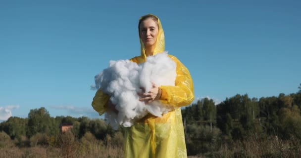 Μια Γυναίκα Κίτρινο Αδιάβροχο Αγκαλιάζει Σύννεφα Από Πολυεστέρα Βάτες — Αρχείο Βίντεο