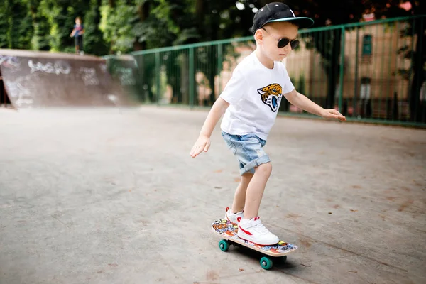 Парень со скейтом в скейт-парке. Мальчик в очках учится кататься на коньках . — стоковое фото