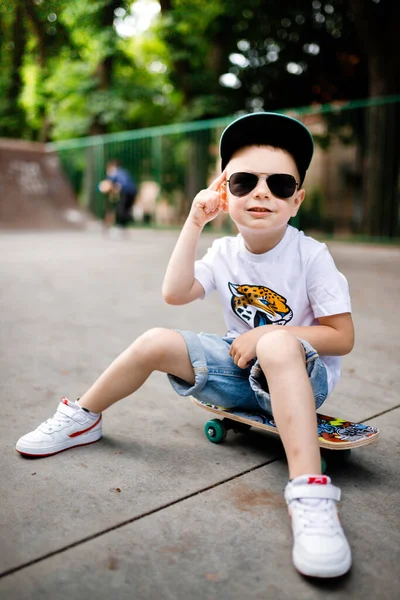 Garçon avec un patin dans un skate park. Le garçon est assis sur une planche à roulettes. — Photo