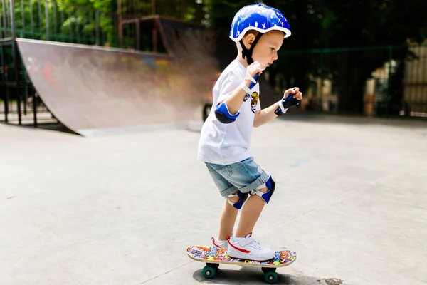 Rapaz com um skate num parque de skate. O menino aprende a patinar, em total proteção . — Fotografia de Stock