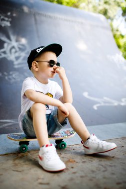 Paten parkında paten yapan bir çocuk. Çocuk kaykayın üzerinde oturuyor..