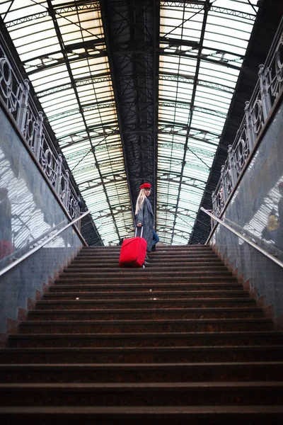Železniční stanice. Krásná dívka stoupá po schodech. Dáma v červené čepici. — Stock fotografie