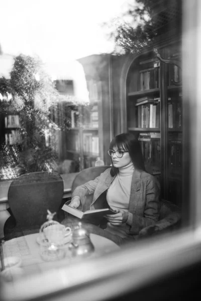 Belle fille rêveuse dans des lunettes nettes élégantes. Dans la bibliothèque. — Photo