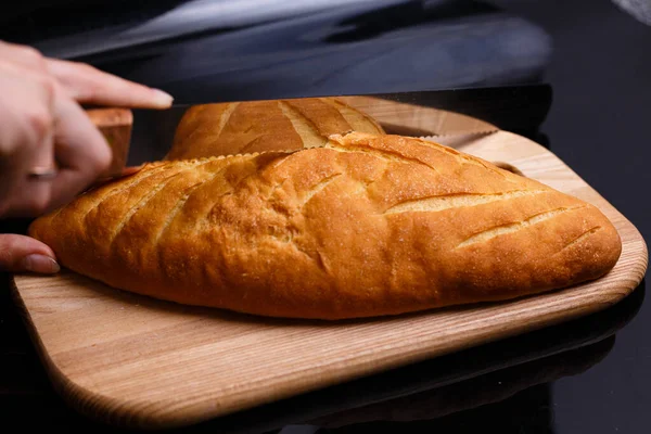 Το σπιτικό άσπρο ψωμί κόβεται με ένα μεγάλο μαχαίρι. Ψήσιμο στο σπίτι. — Φωτογραφία Αρχείου