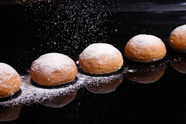 Baking on a black background. White buns sprinkled with powder and flour.