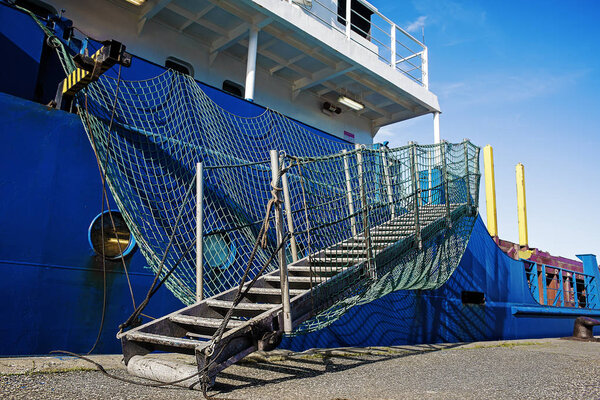 Stern of cargo vessel at port. Gangway arrangment. Blue hull. White superstructure.