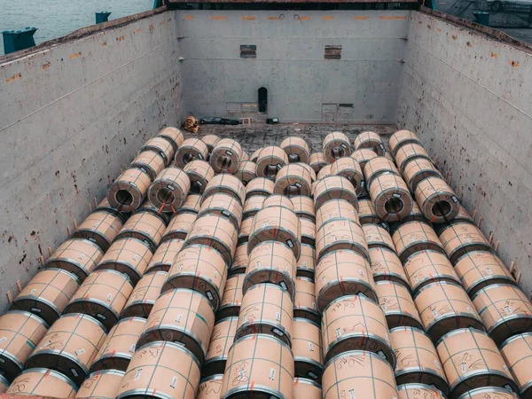 Loading steel coils from shore to the cargo vessel. Stevedors are working in cargo hold.