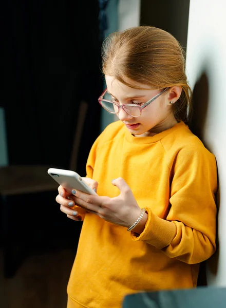 一个穿着黄色毛衣的女孩手里拿着智能手机。儿童过度使用智能手机的问题 图库图片