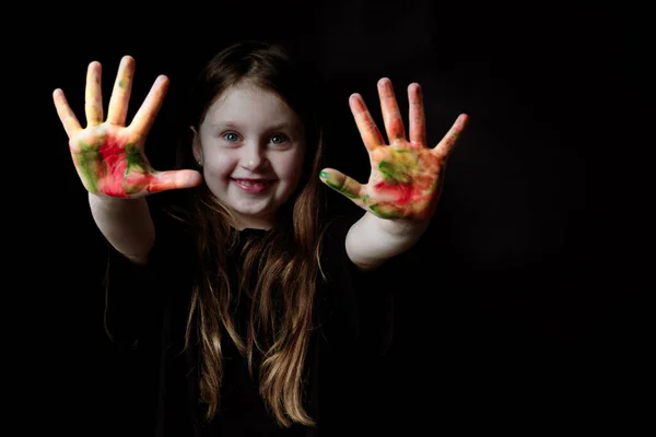 A menina em uma camiseta preta e longo cabelo solto sorri e mostra suas mãos pintadas . Imagens Royalty-Free
