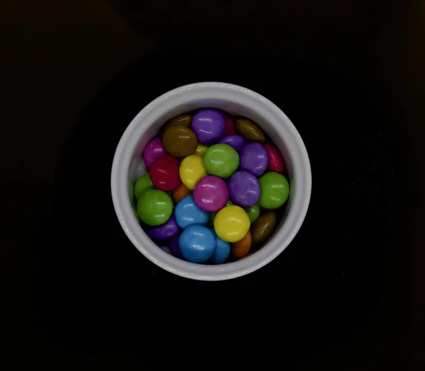 Farbige Bonbons im weißen Topf vor schwarzem Hintergrund — Stockfoto