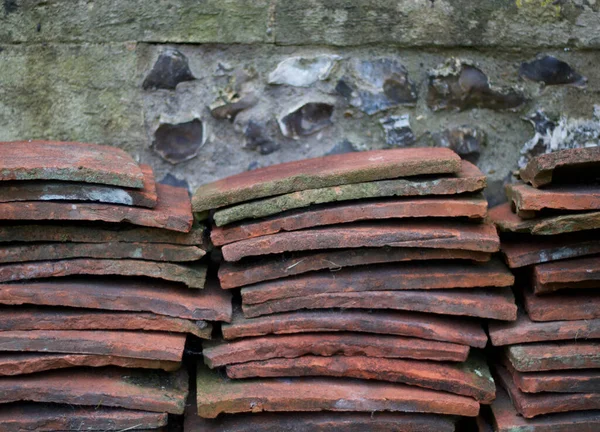 Stacks of old terracotta roof tiles piled against weathered flint wall — Stock Photo, Image