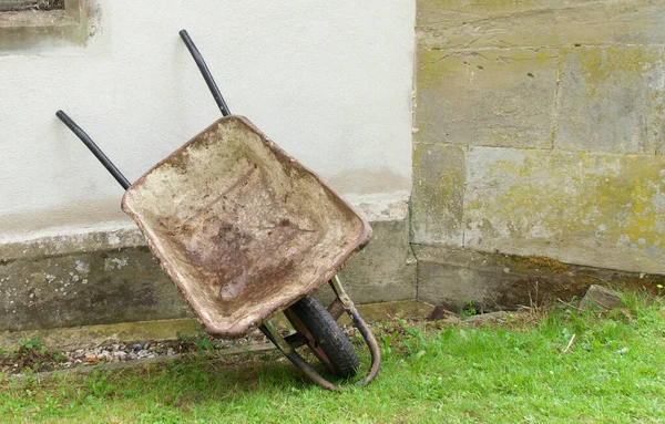 Yaşlı inşaatçılar el arabaları duvara yaslanır ve çimlerin üzerinde dururlar.