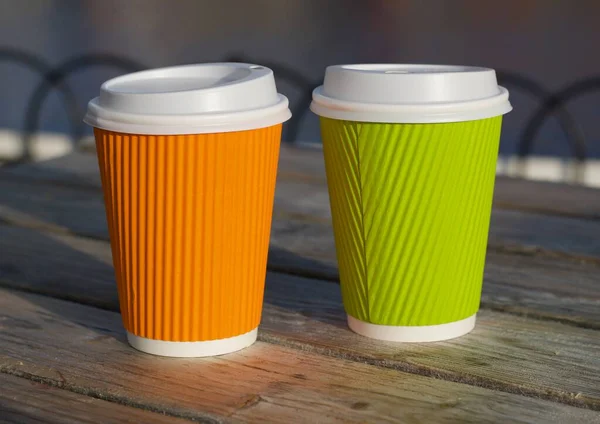 Two insulated cups in orange and green standing on wooden table — Stock Photo, Image