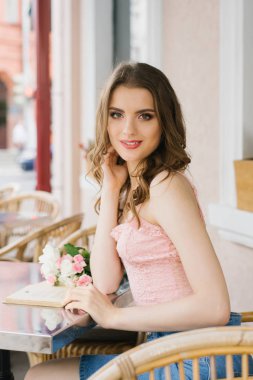 güzel bir makyaj ile romantik genç kız bir sokak kafenin bir masada bir kitap okur. Masada onun yanında bir buket gül var. kitap okuma kavramı