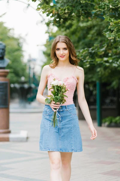 街を歩く美少女の肖像画 ピンクと白のバラの花束を持つ若い笑顔の女性 夏の街の背景 — ストック写真