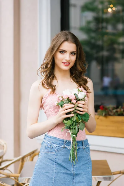 Şehirde bir yaz kafenin terasında elinde gül bir buket ile güzel bir gülümseyen kız yaz portresi