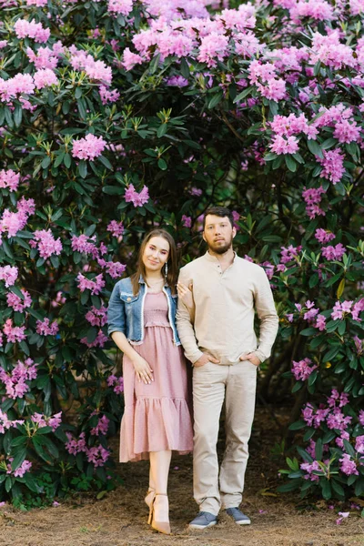 beautiful young couple girl and the guy stand on the background of a blooming rhododendron. portrait of a happy young family