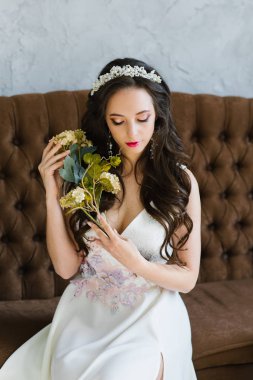 Beyaz bir gelinlik içinde saçları aşağı ile gelin çiçek bir buket tutan. Profesyonel makyaj ile hassas esmer portre.
