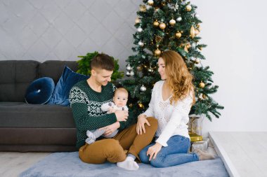 Noel için dekore oturma odasında mutlu bir gülümseyen ve neşeli bir ailenin portresi. Baba kucağında çocuk tutan, anne onlara bakar ve gülümsüyor. Aile yerde oturuyor. Chri yeni yılı kutlayan konfor kavramı