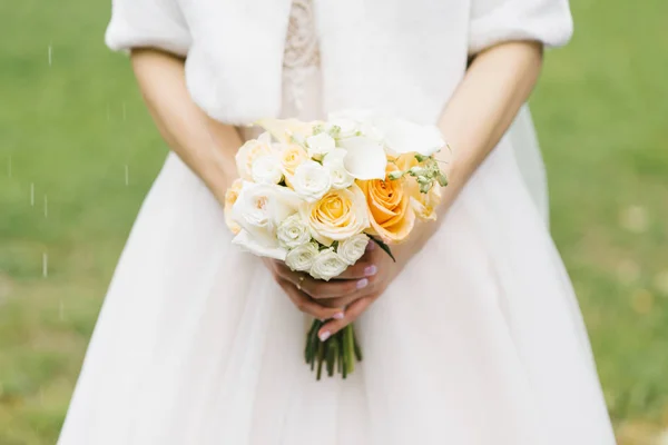 White and orange wedding bouquet in the hands of the bride