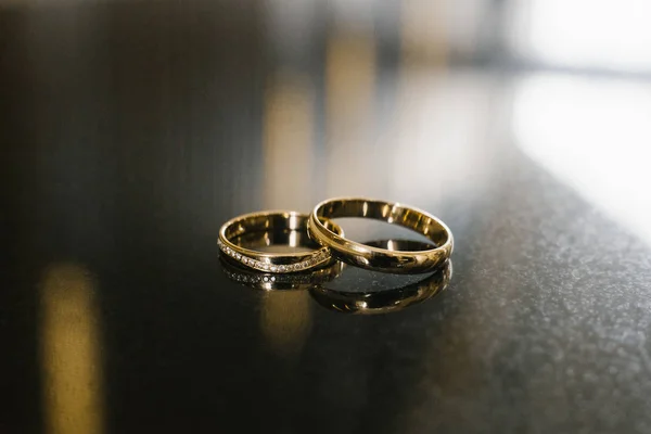 gold wedding rings at the wedding, the bride\'s diamond ring lie on a brown gray surface, macro