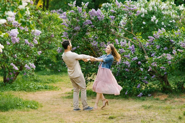 Jovem Casal Amoroso Mãos Dadas Girando Jardim Lilás Primavera Sorrindo — Fotografia de Stock