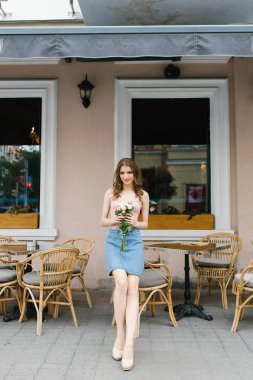 Güzel, kahverengi saçlı, uzun bacaklı, gül buketli, profesyonel makyajlı genç bir kız. Romantik ve nazik bir imaj. Sokak kafesinin masalarında bekliyorum.